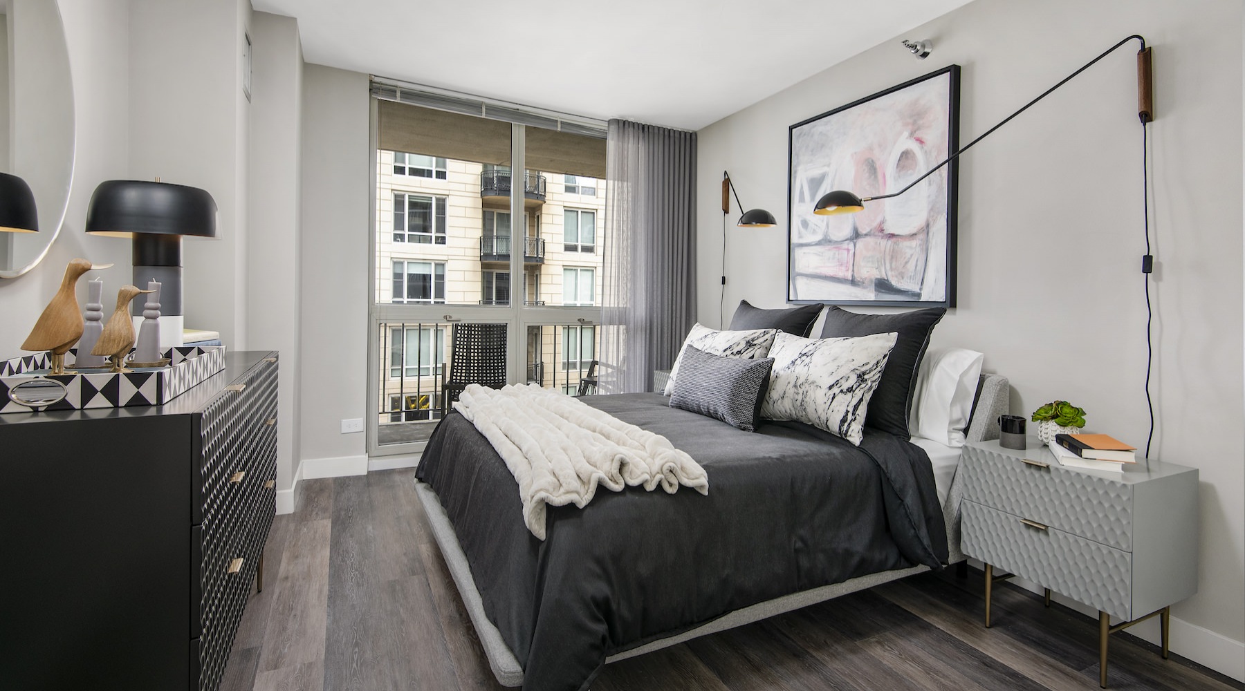 Large well lit bedroom with wood floors and a large window 