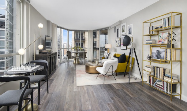 Spacious and well lit living room with wood flooring, large windows and open access to the kitchen.